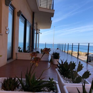 A balcony with potted plants, a view of the sea, and a building with large windows. - Salento Palace Bed & Breakfast (Gallipoli)
