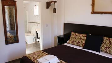 A hotel room with a large bed, a bedside table, a mirror, and a bathroom visible through an open door.