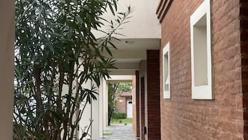 A narrow brick corridor with white-framed windows, leading to a covered outdoor area.