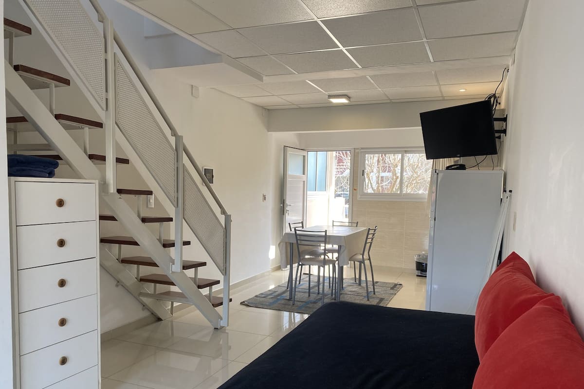 Ein Schlafzimmer mit Bett, Schreibtisch und Stuhl. Eine Treppe führt in einen anderen Raum.