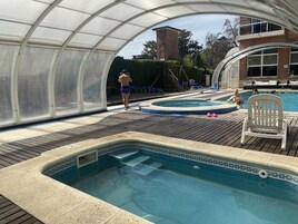 Una piscina exterior cubierta con jacuzzi, terraza de madera y zona de estar techada.