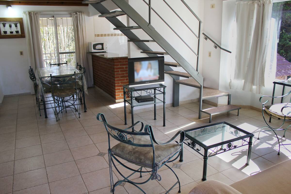 Ein Wohnzimmer mit Fernseher, Esstisch, Stühlen und einer Treppe.