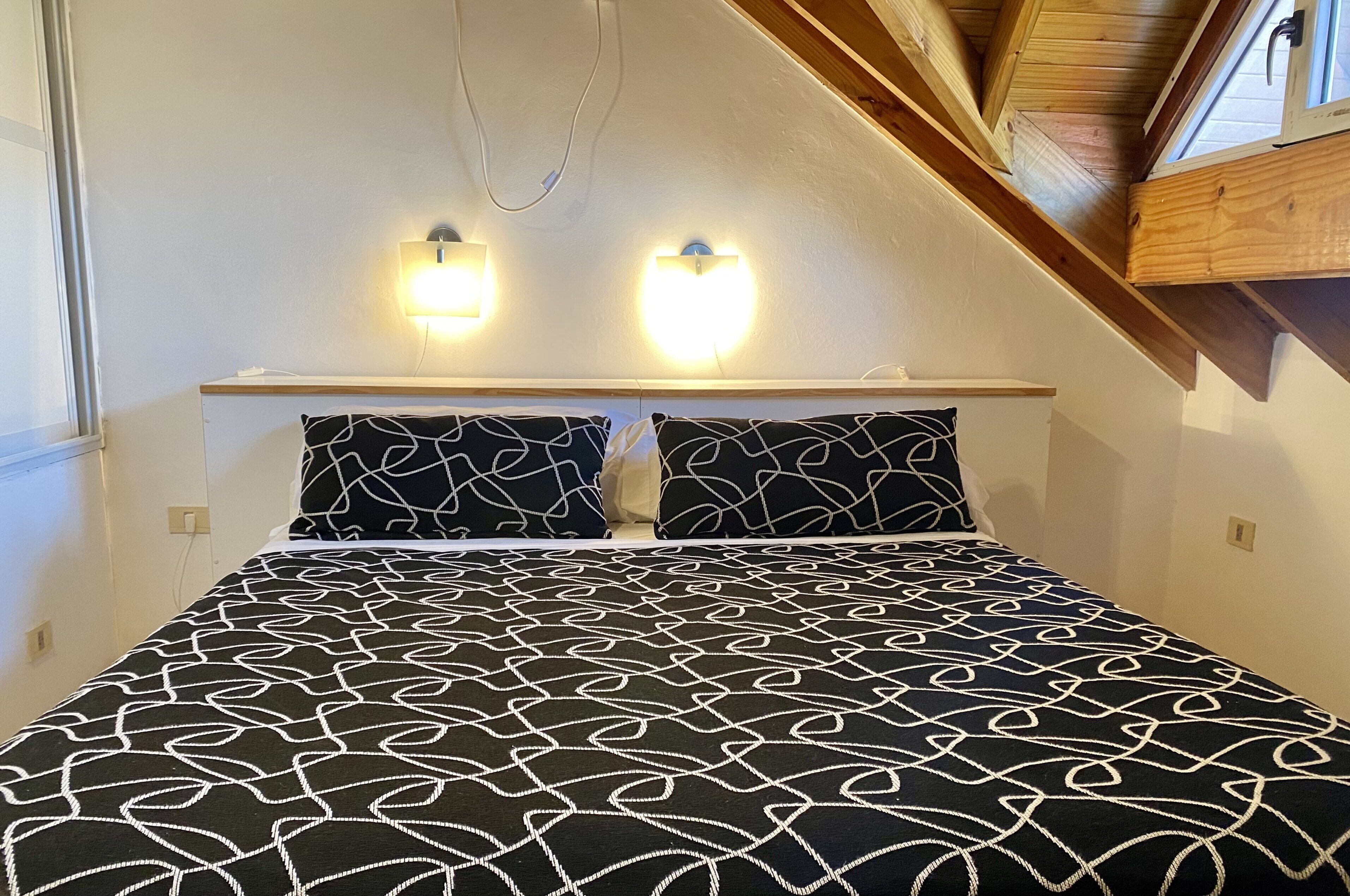 Un dormitorio con una cama, dos luces empotradas y un techo inclinado.