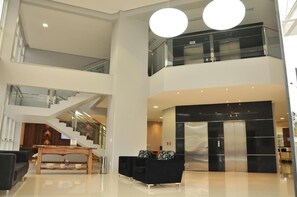 Un hall d’entrée spacieux avec un escalier, un comptoir d’accueil et un ascenseur moderne.