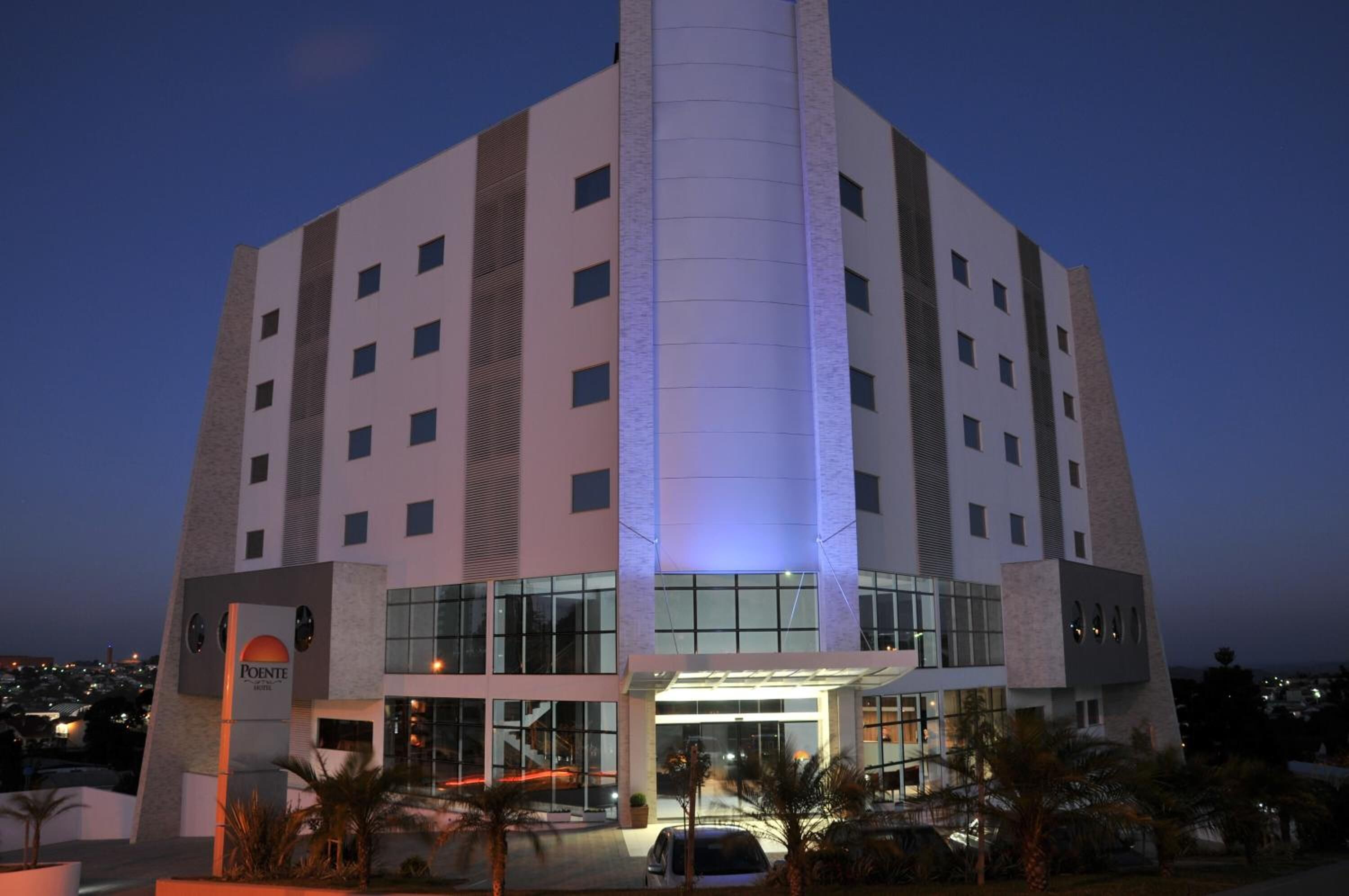 A modern hotel with a central tower, multiple floors, and a well-lit entrance.