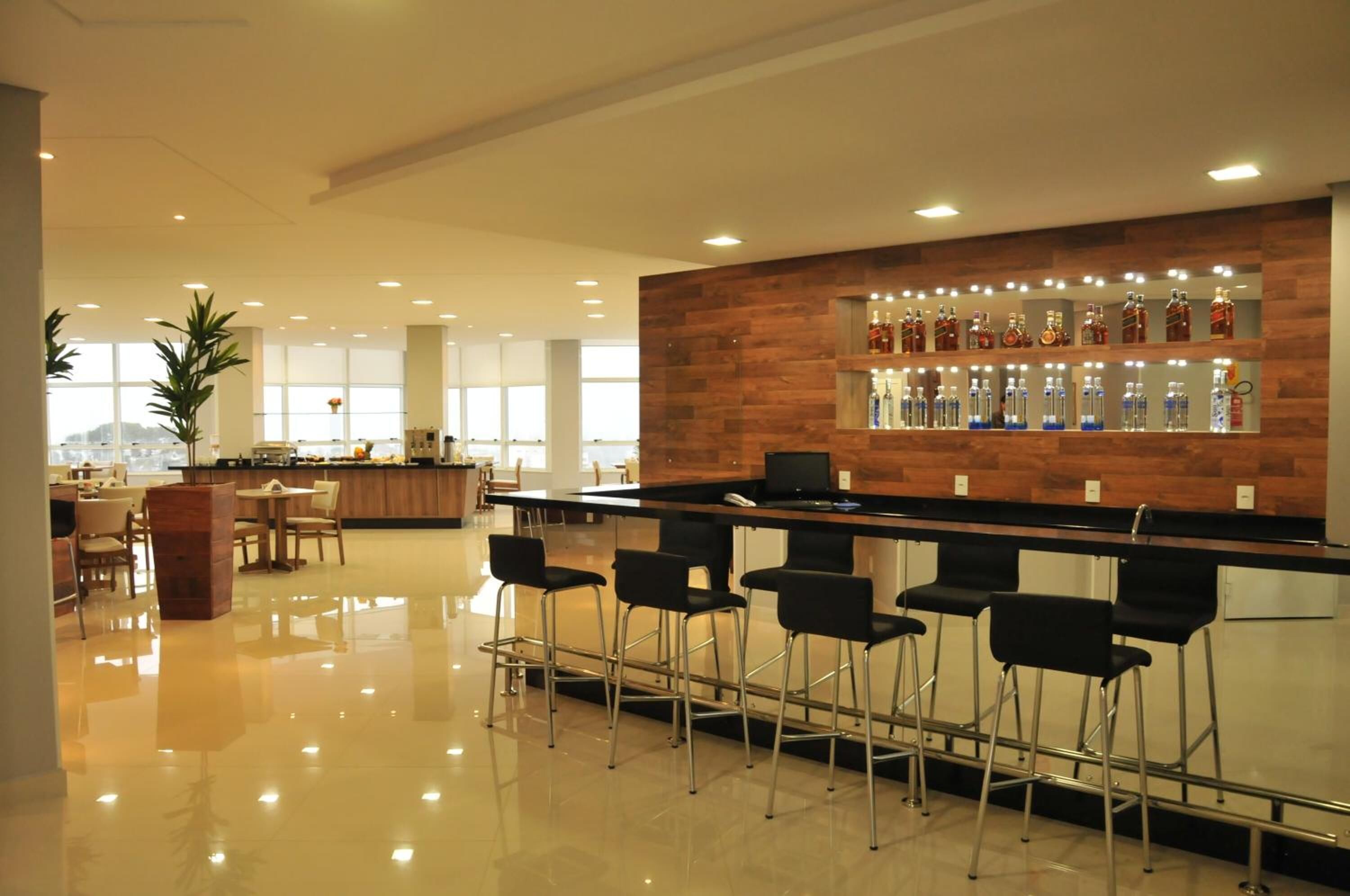 A modern bar area with a wooden accent wall, bar stools, and a variety of bottles.