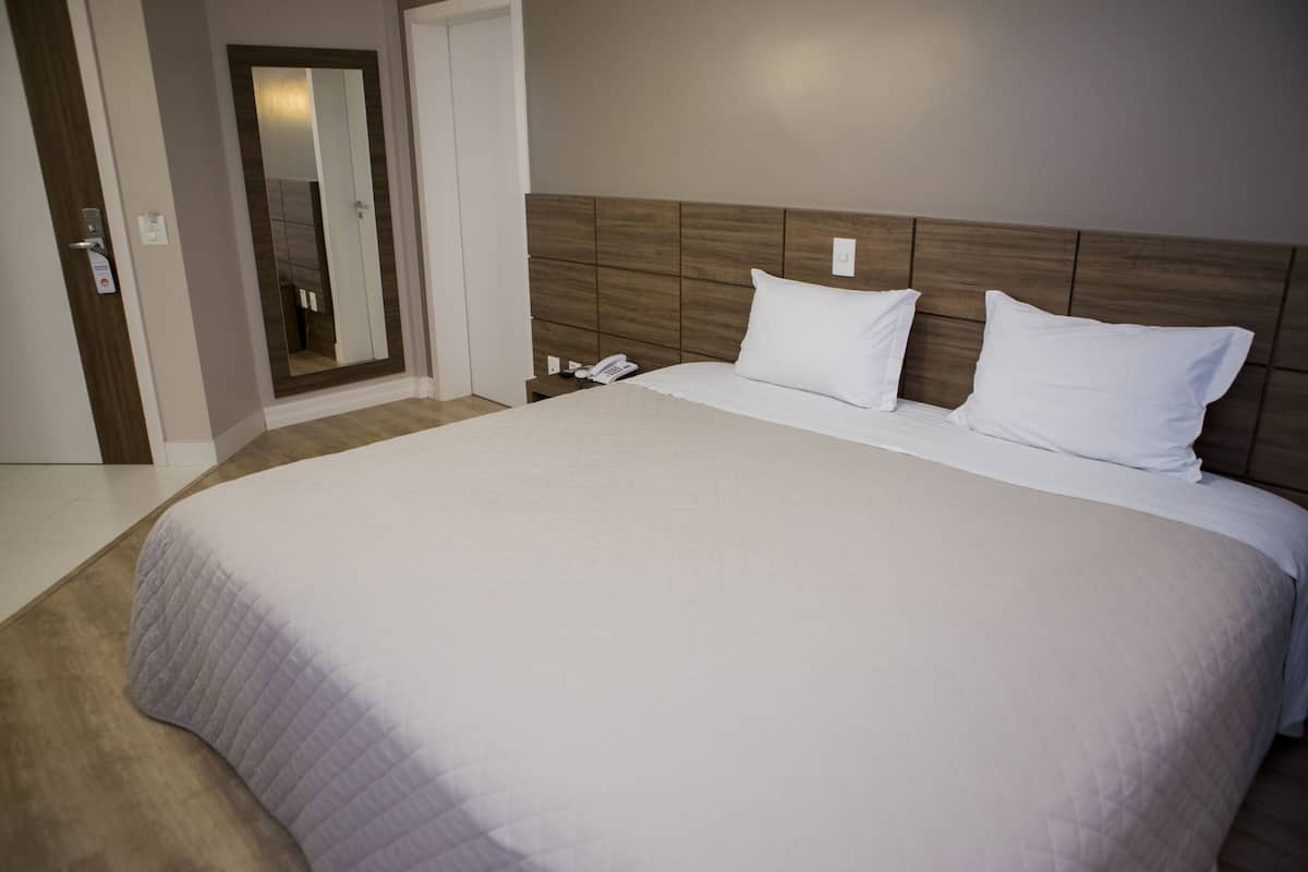 Habitación de hotel con una cama grande, un cabecero de madera, una mesita de noche con un teléfono y un espejo.