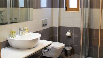A modern bathroom with a large mirror, a white sink, a toilet, and a glass-enclosed shower.