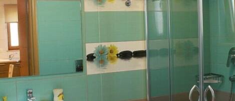 A bathroom with a glass-enclosed shower, a sink with a mirror, and decorative tiles.