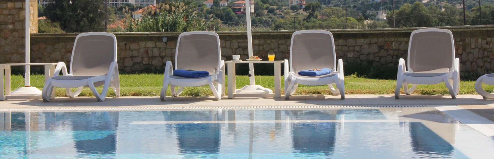 Zona de piscina amb gandules i una taula amb una beguda.
