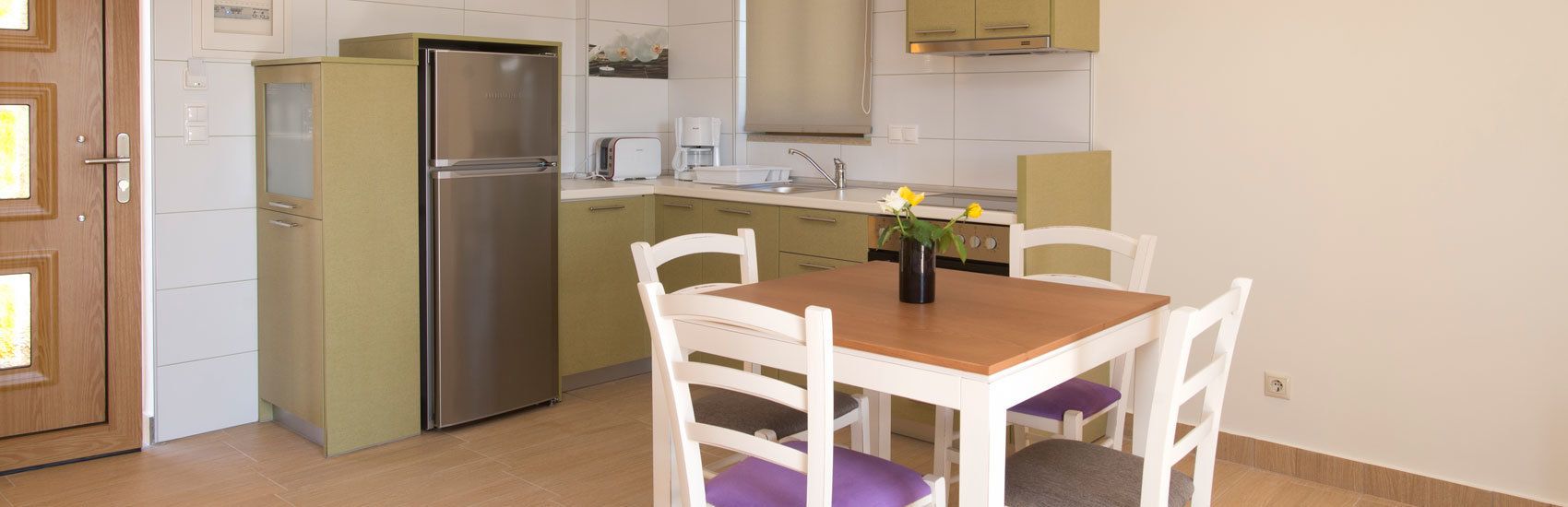 Una cocina compacta con refrigerador, cafetera y una mesa de comedor con sillas.