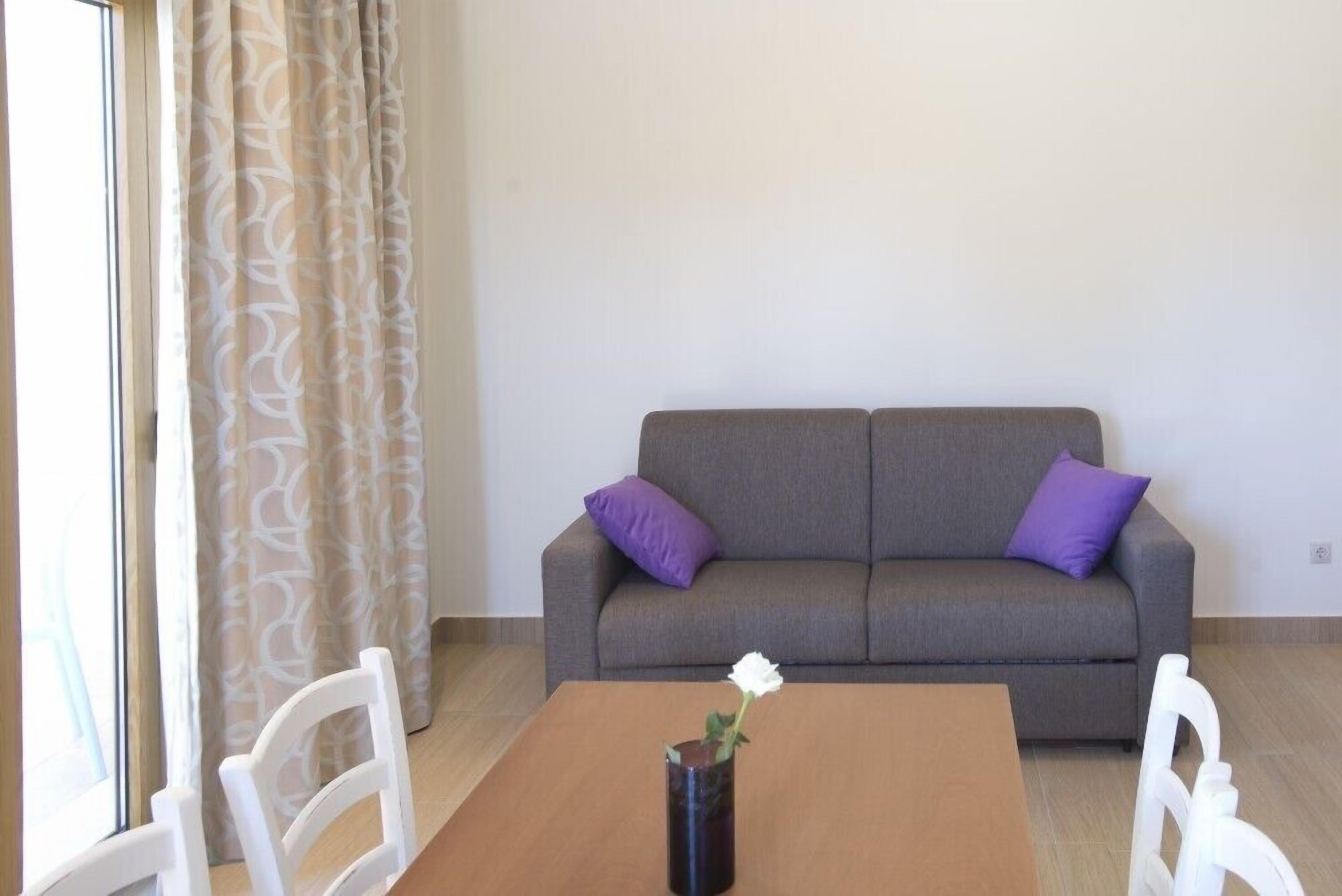A room with a grey sofa, two purple cushions, a wooden table, and a white chair.