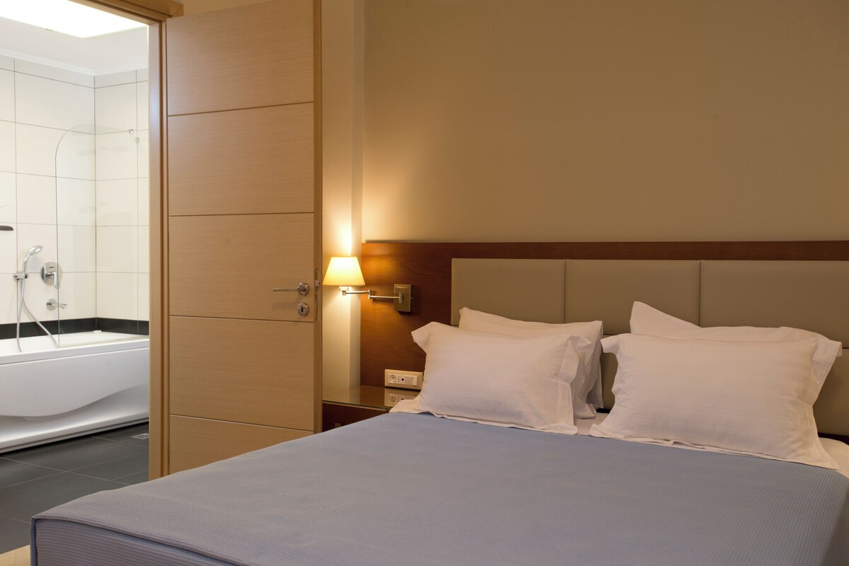 A hotel room with a bed, a nightstand, a lamp, and a bathroom with a bathtub.
