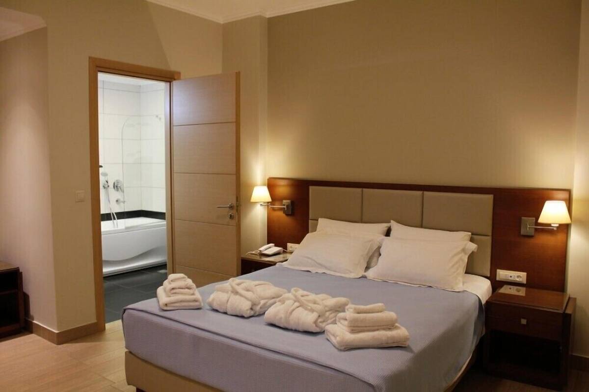 A hotel room with a bed, two bedside tables, a nightstand, a bathroom with a bathtub, and towels on the bed.