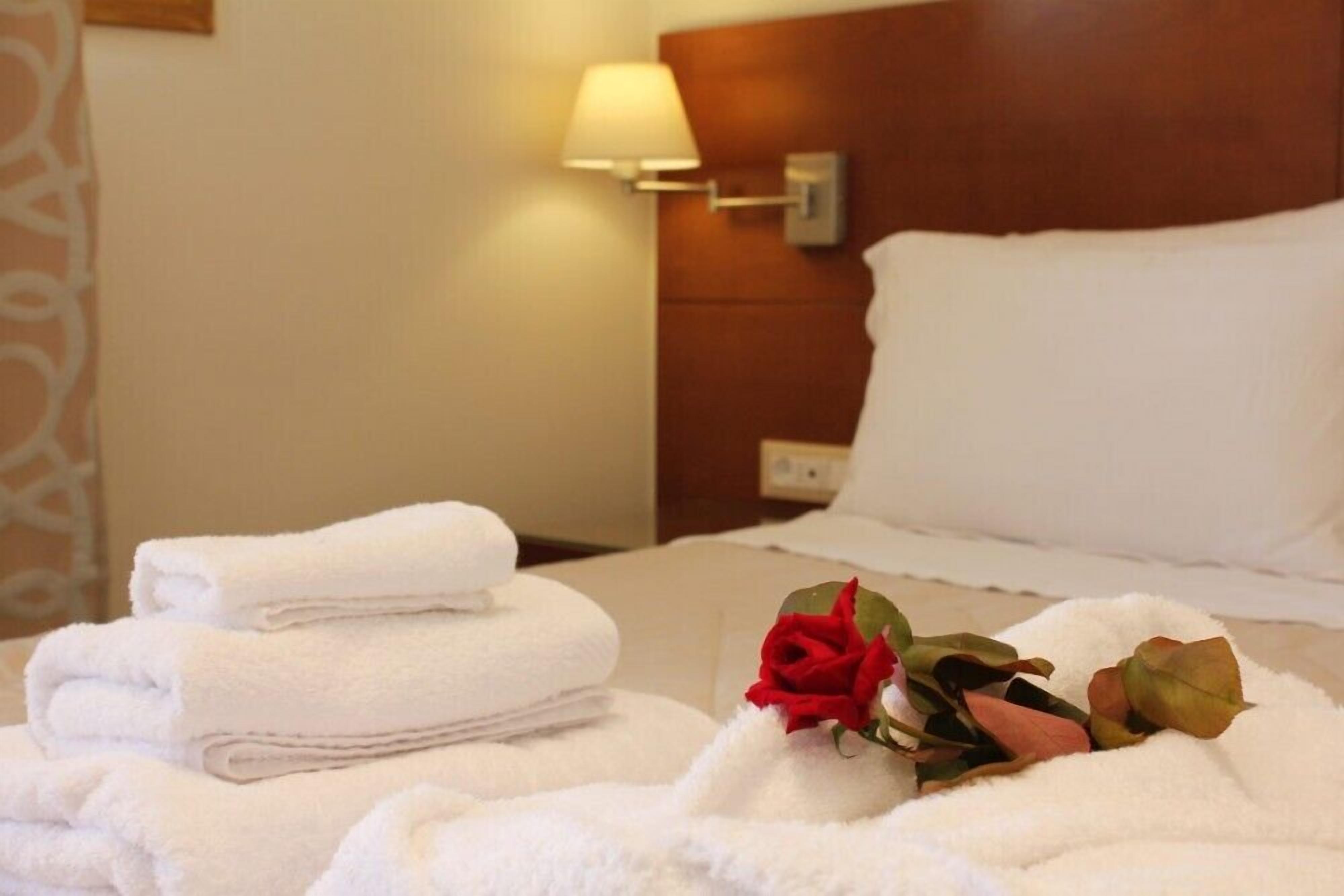 A neatly made bed with white linens and a red rose decoration.