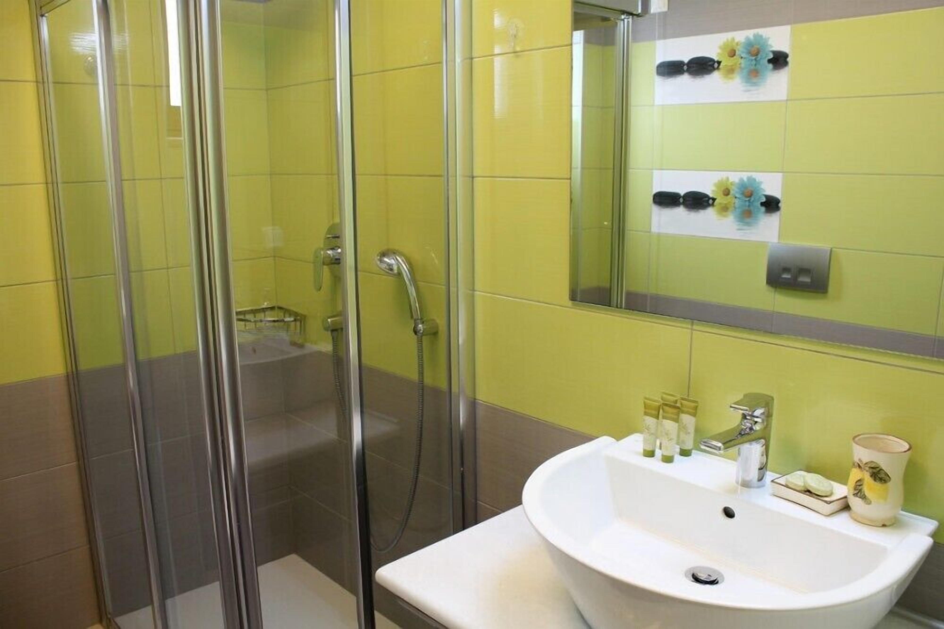 Un baño con cabina de ducha de vidrio, un lavabo blanco y un espejo con diseño floral.