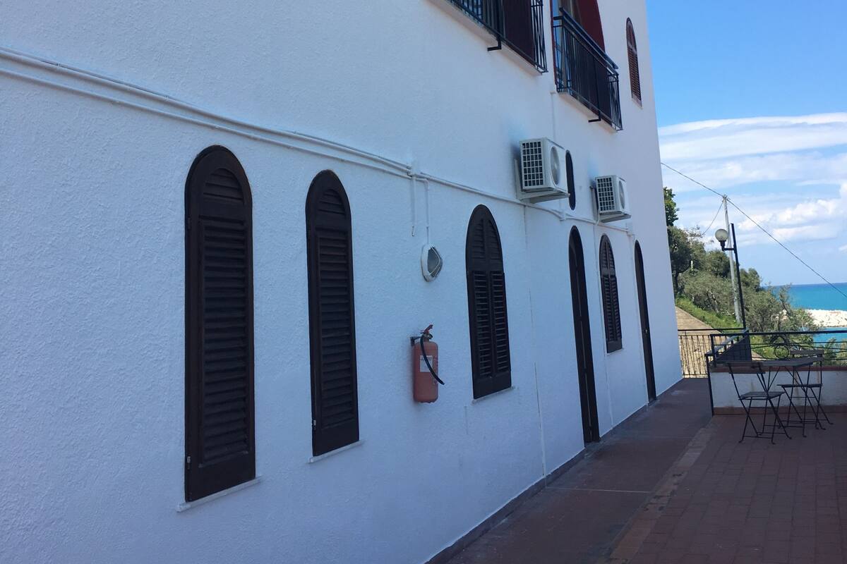 A white building with arched windows and balconies, a fire extinguisher, and a view of the sea.