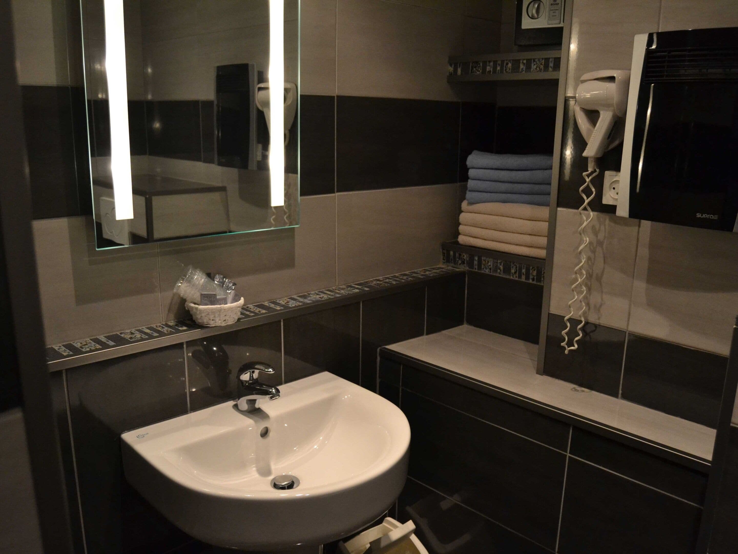 Une salle de bain moderne avec un lavabo blanc, un miroir en verre et un porte-serviettes sur lequel sont pliées des serviettes.