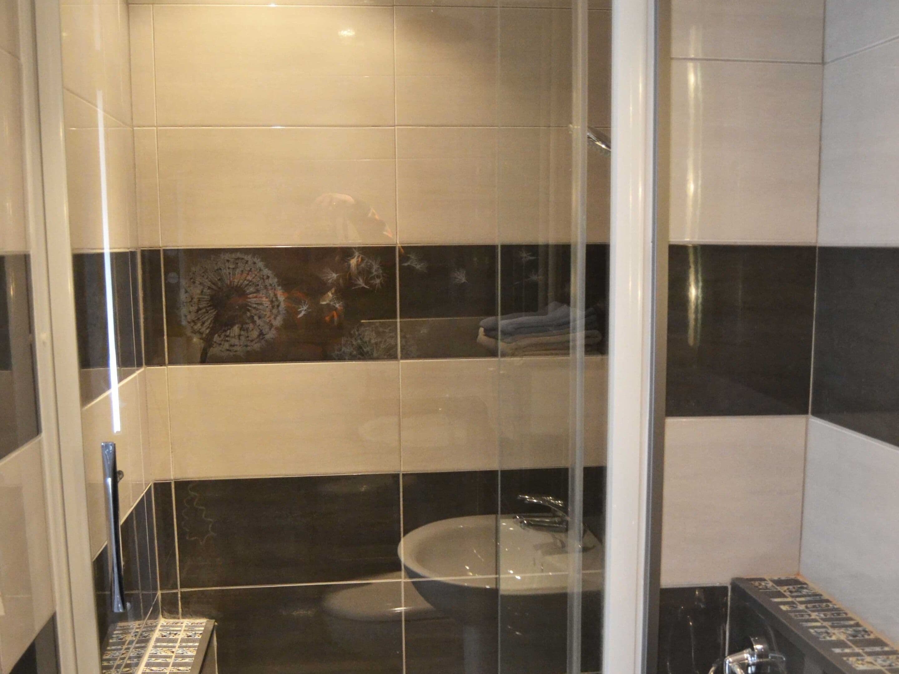 A bathroom with a glass shower enclosure, a toilet, and a sink.