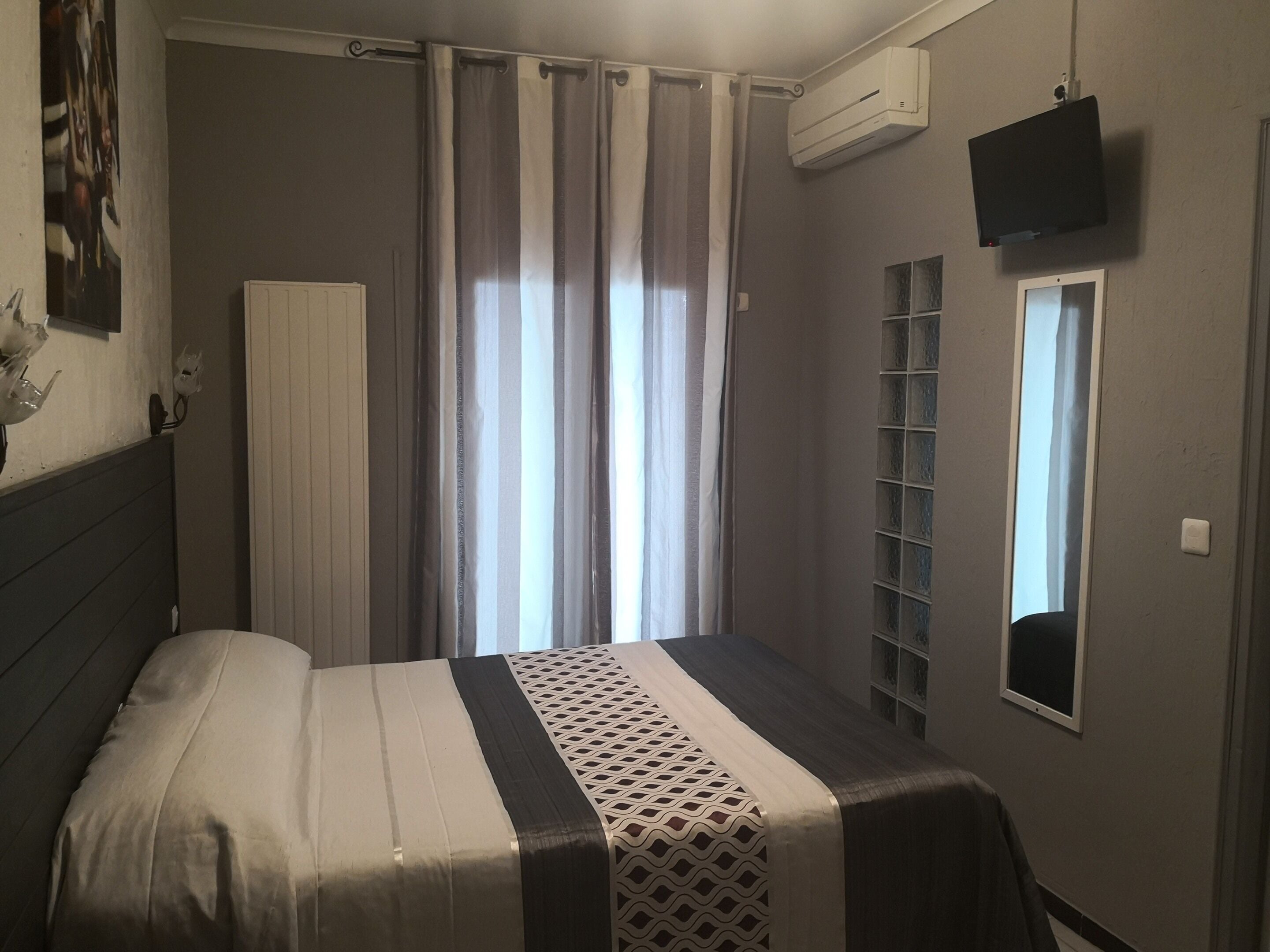 Un dormitorio con cama, cortinas, aire acondicionado, televisor y una ventana pequeña.