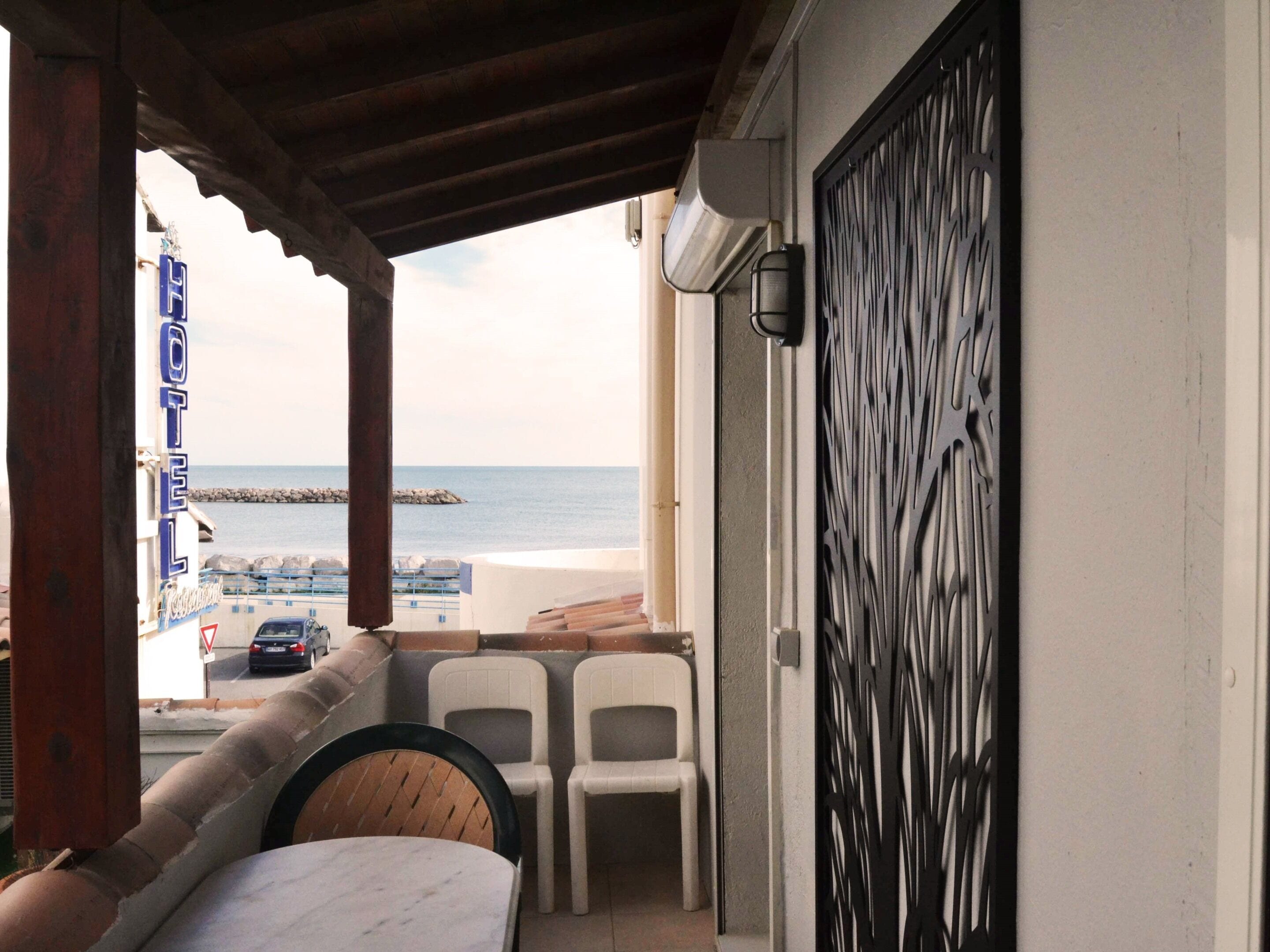 Un balcón con vista al mar, sillas de plástico blanco y una mesa.