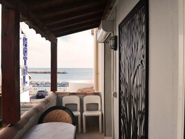 Uma varanda com vista para o mar, cadeiras de plástico branco e uma mesa.