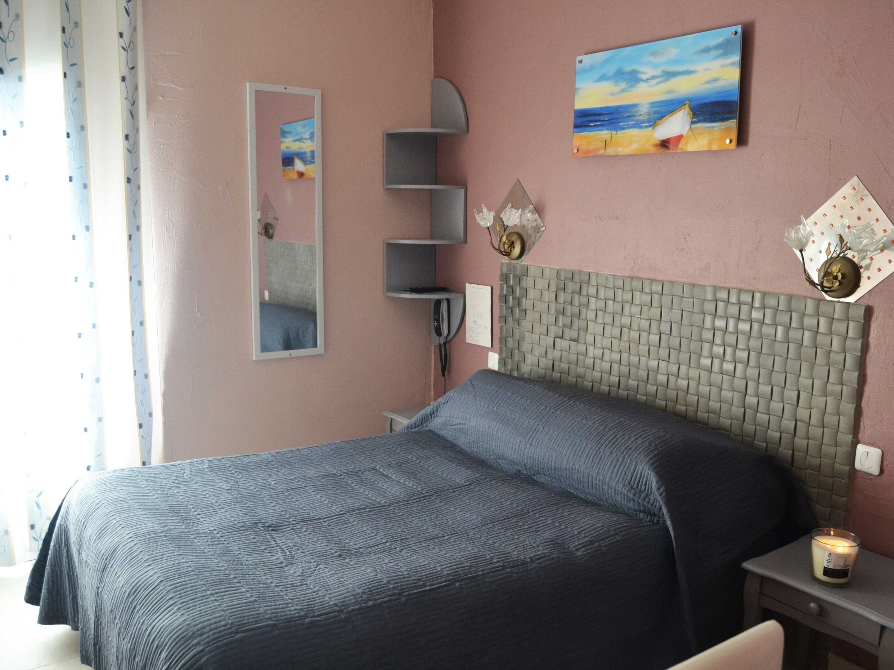 A bedroom with a bed, a bedside table, a nightstand, a mirror, a painting, and a wall-mounted shelf.