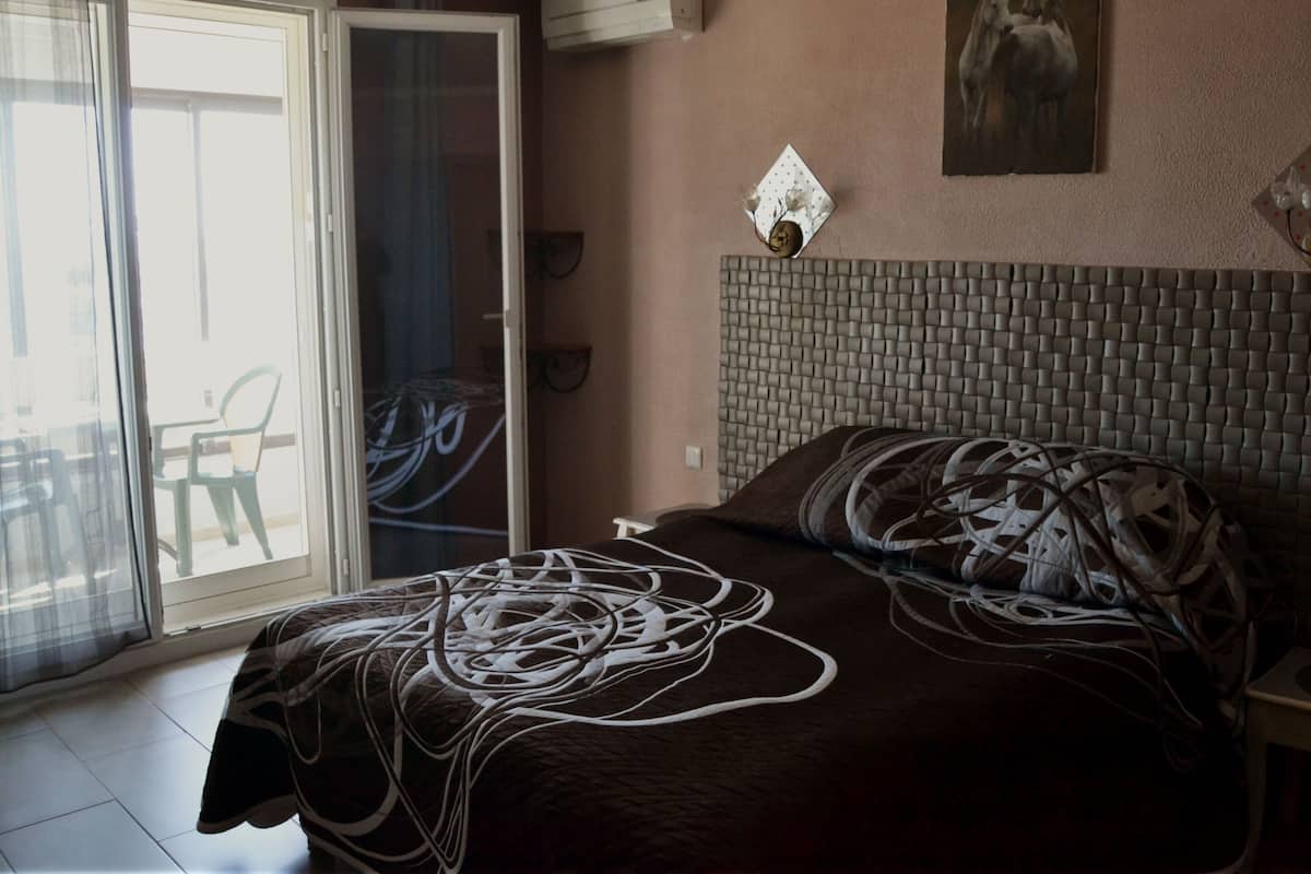 A bedroom with a bed, a painting, a wall-mounted light, and a sliding glass door leading to an outdoor area.