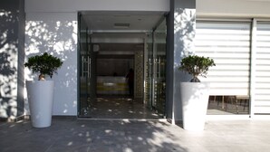 A modern building entrance with a reception desk, glass doors, and potted plants. - Flora Maria Hotel (Ayia Napa)