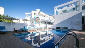 A rooftop pool with blue lounge chairs and umbrellas, surrounded by white buildings with balconies. - Flora Maria Hotel (Ayia Napa)