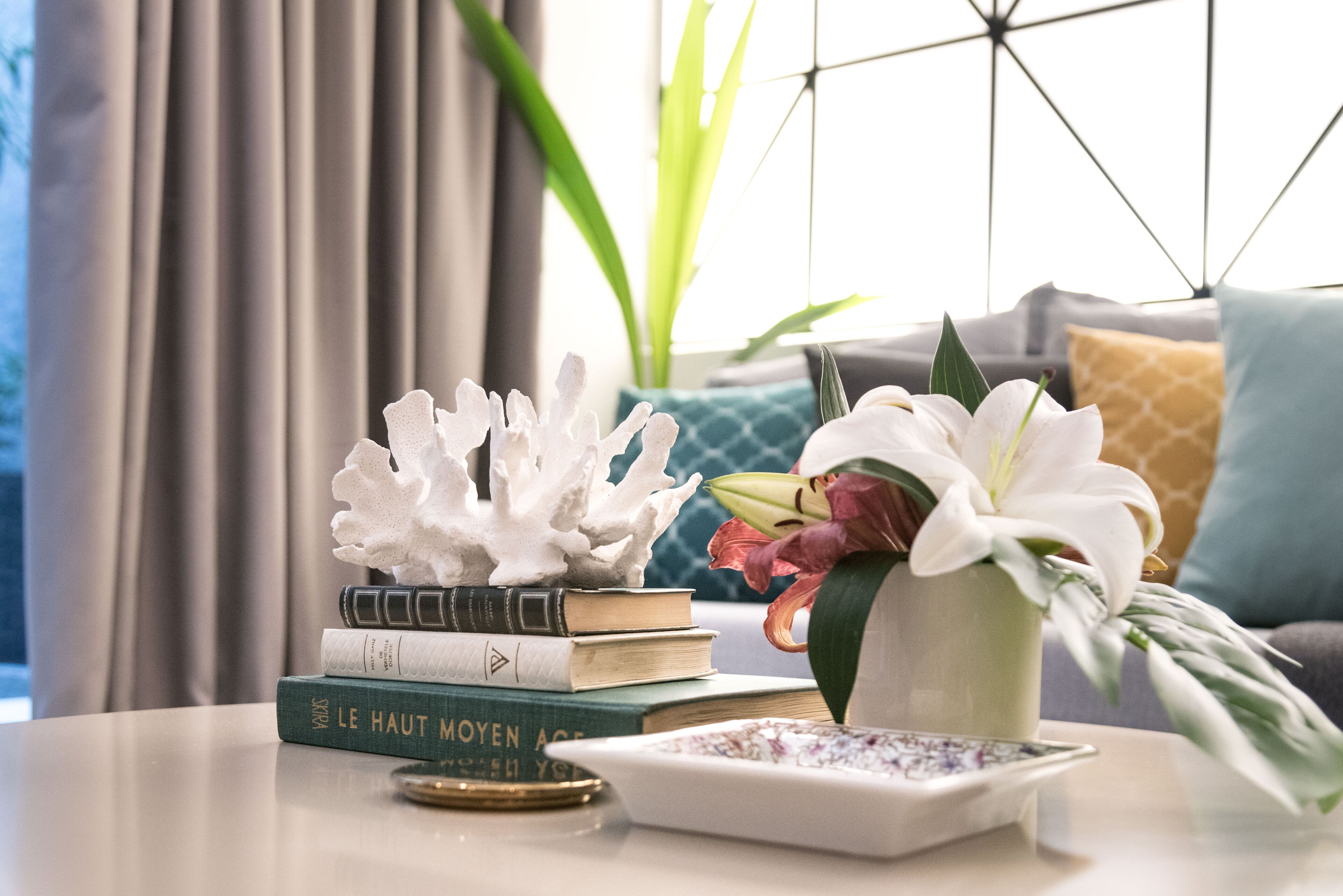 Ein ordentlich gedeckter Tisch mit Büchern, einem dekorativen Korallenstück, einer Blumenvase und einem kleinen Teller.
