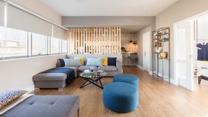 A modern living room with a sectional sofa, ottomans, a coffee table, and a kitchen area in the background. - 47 Luxury Suites (Athens)
