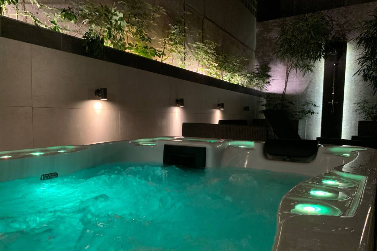 Ein Whirlpool mit Wasserfall, umgeben von gefliesten Wänden und Blumentöpfen.