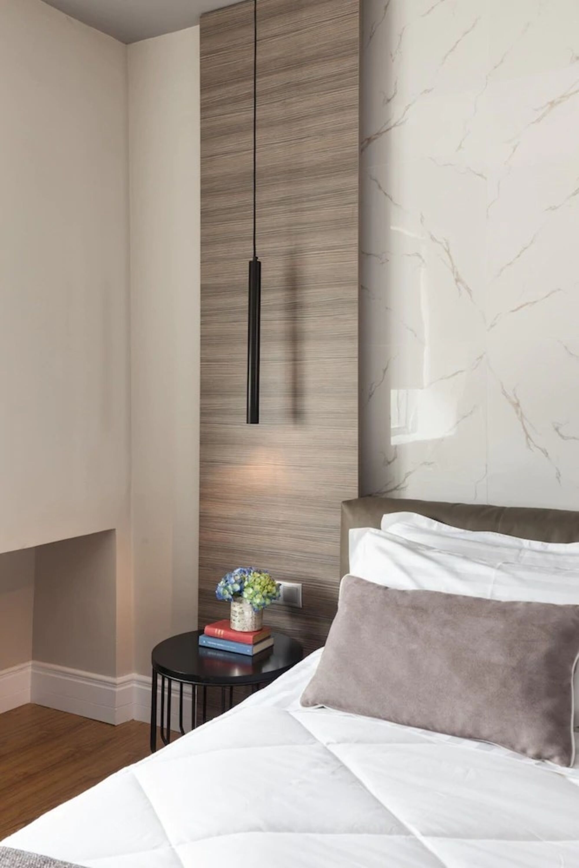 Un dormitorio moderno con cama, mesita de noche, lámpara de pared y pared con diseño de mármol.