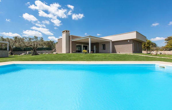 A modern house with a swimming pool, a covered patio, and a stone wall in the background.