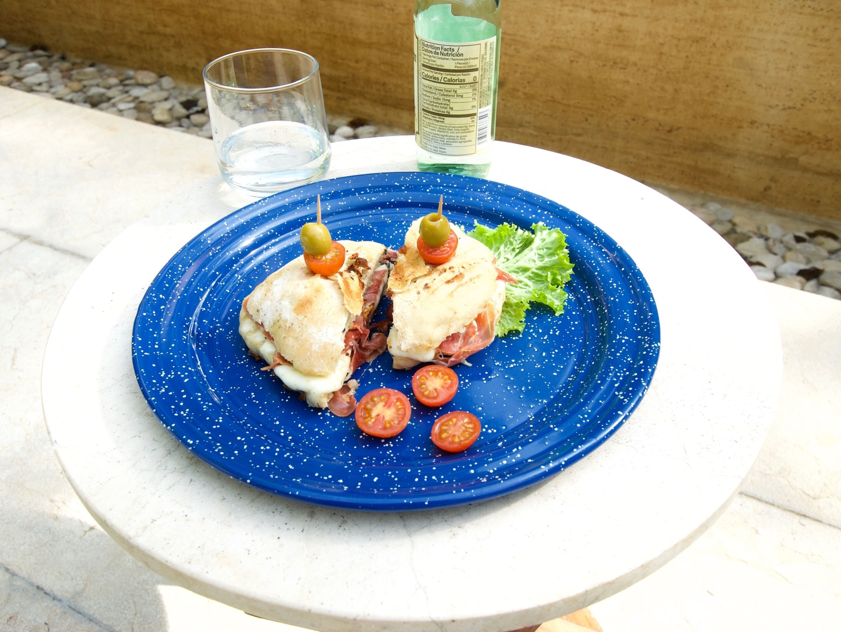 A plate with a sandwich, a glass of water, and a bottle of water on a white table.