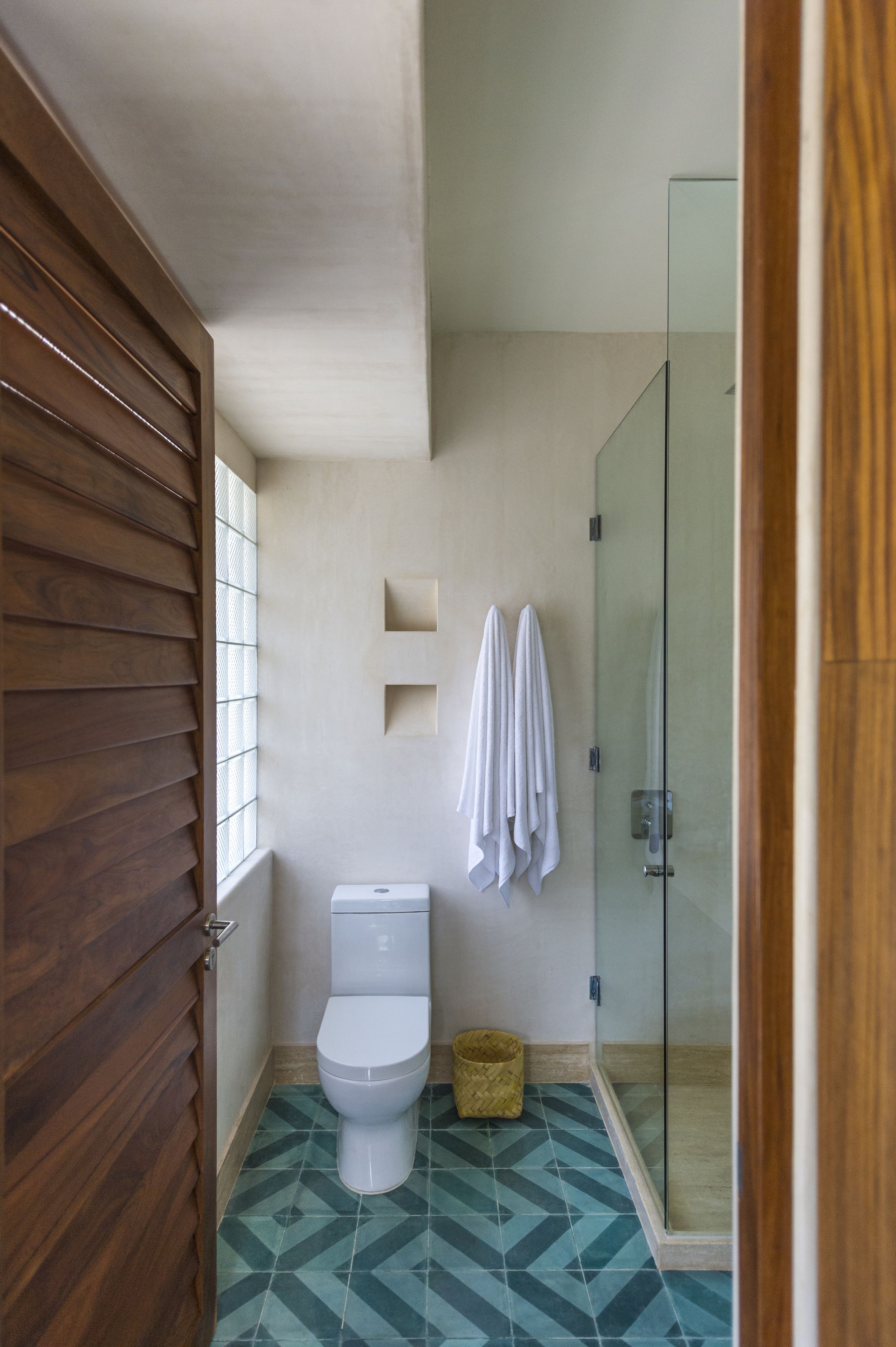 A bathroom with a wooden door, a toilet, a glass shower enclosure, and a patterned floor.