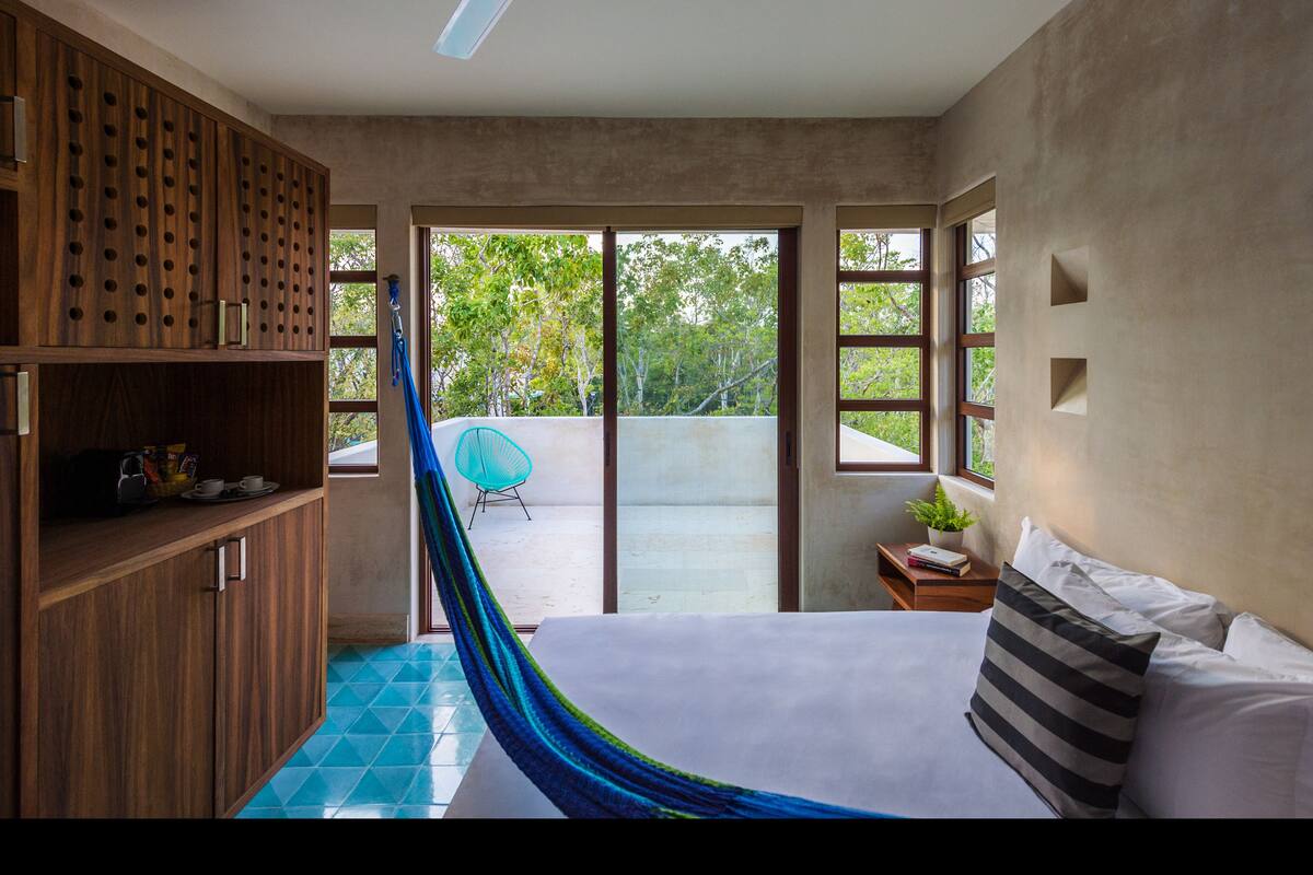 Une chambre avec un lit, un hamac, une chaise et une vue sur la verdure.