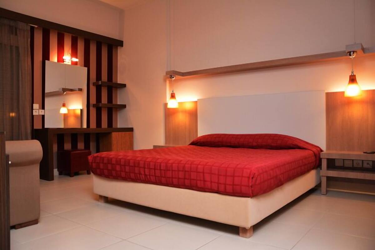 A bedroom with a large bed, a wooden headboard, a bedside table, a mirror, and a small stool.