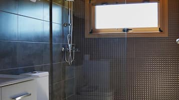 Een moderne badkamer met een glazen douchecabine, een toilet en een raam boven de wastafel.