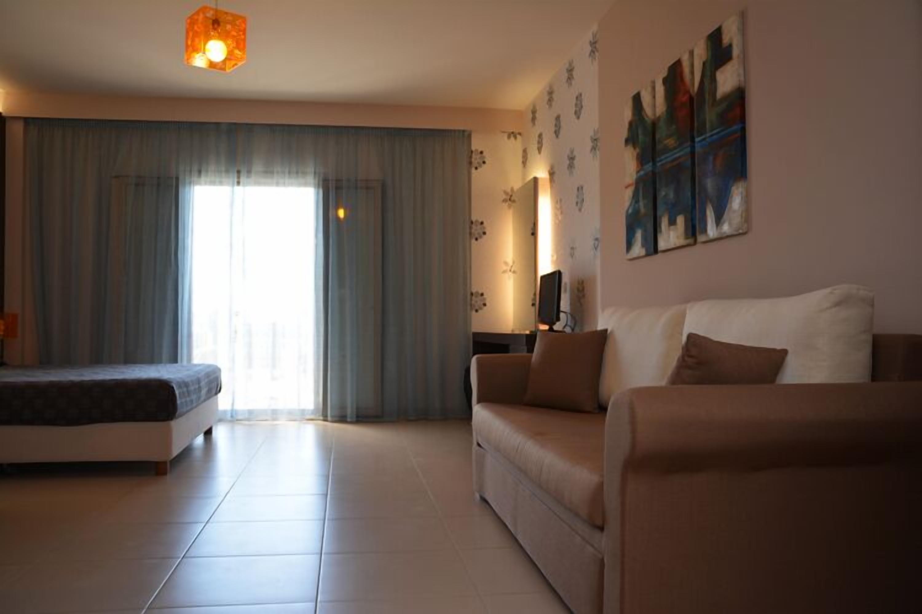 A spacious living room with a sofa, a bed, and a large window with curtains.