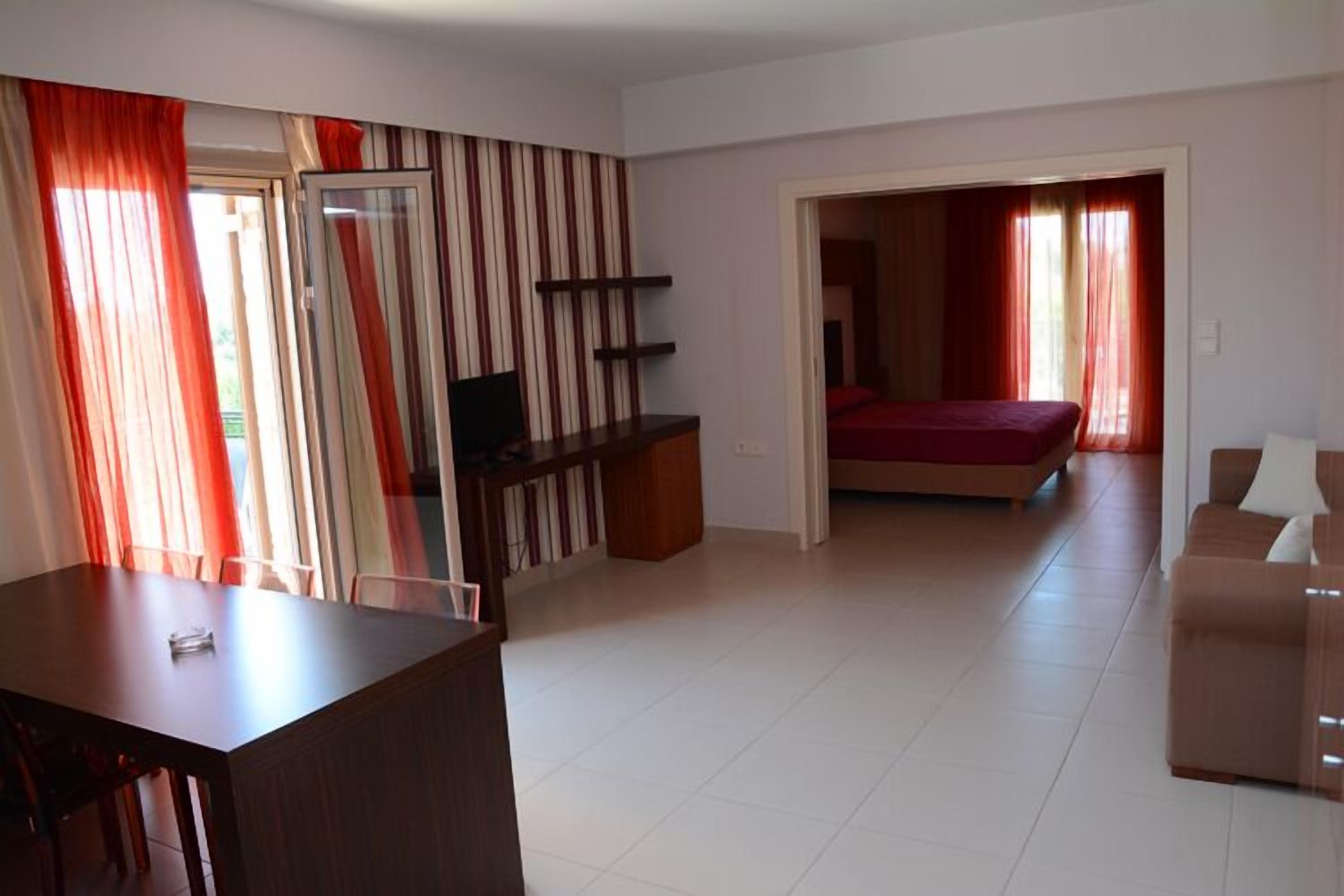 A modern room with a bed, a desk, and a TV. There is a door leading to another room.