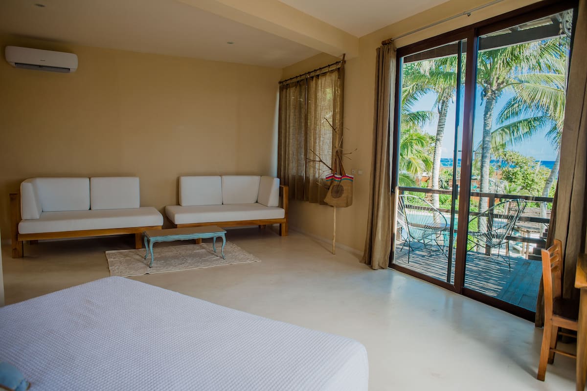 A room with a bed, two sofas, a small table, and a view of a pool and palm trees through large sliding doors.