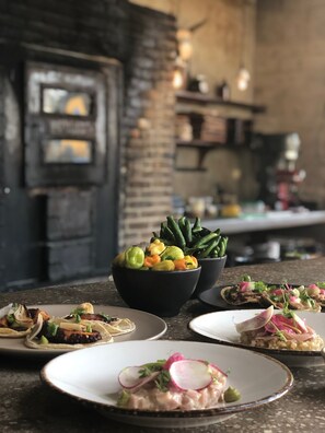 A dining area with a rustic brick wall, a black bowl of mixed vegetables, and plates of food.