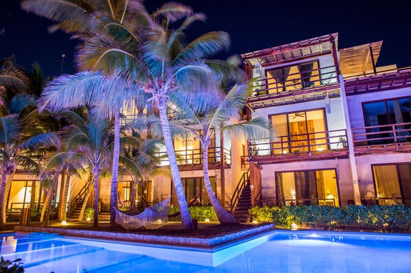 A modern hotel with a pool, palm trees, and a well-lit exterior at night.