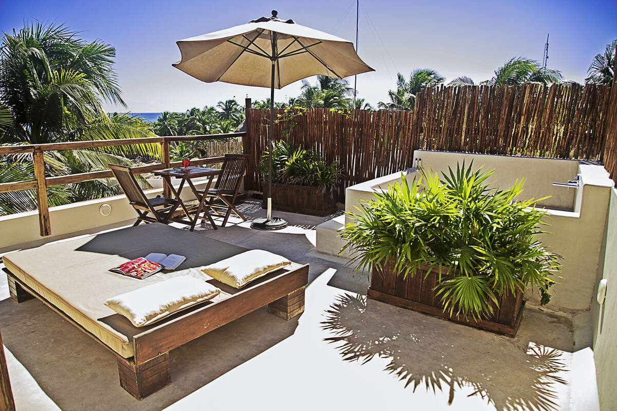 A rooftop terrace with a bed, lounge chairs, an umbrella, and potted plants.
