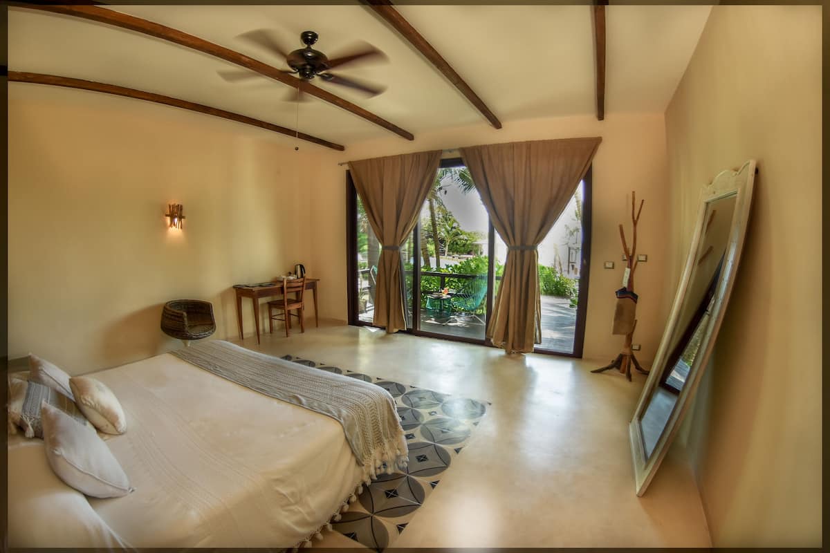 A bedroom with a bed, a ceiling fan, a desk, and a large window with curtains.