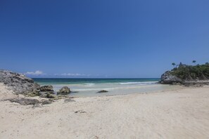 A beach with clear blue water, rocky outcrops, and sparse vegetation.