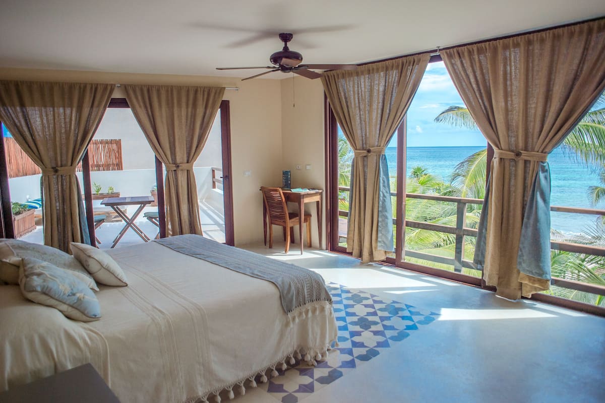 A bedroom with a bed, a desk, and a view of the ocean.