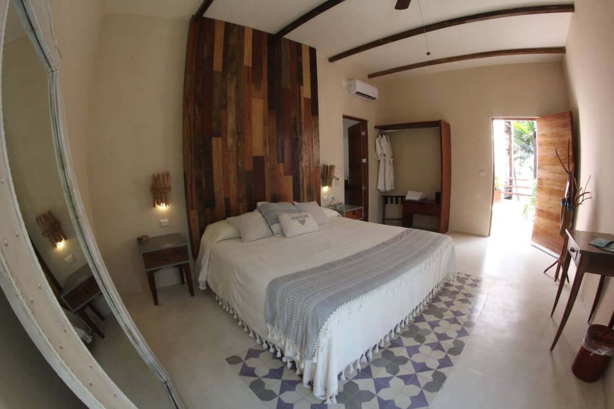 A bedroom with a large bed, wooden panel wall, bedside tables, a mirror, and a bathroom with a shower and toilet.